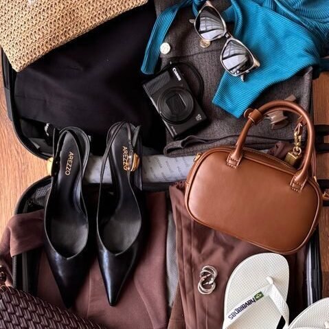Seasonal & Weather-Focused Flat lay of fashion and travel essentials in an open suitcase on wooden floor, ready for vacation.