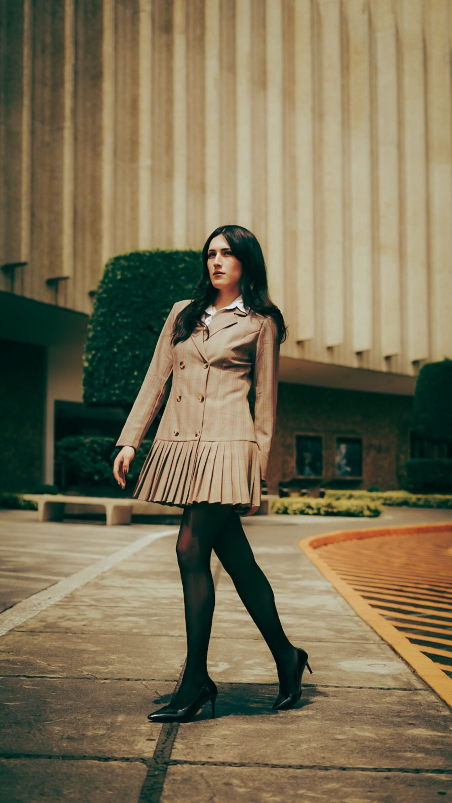 Seasonal & Weather-Focused Stylish woman in a formal dress walking confidently by a modern building.